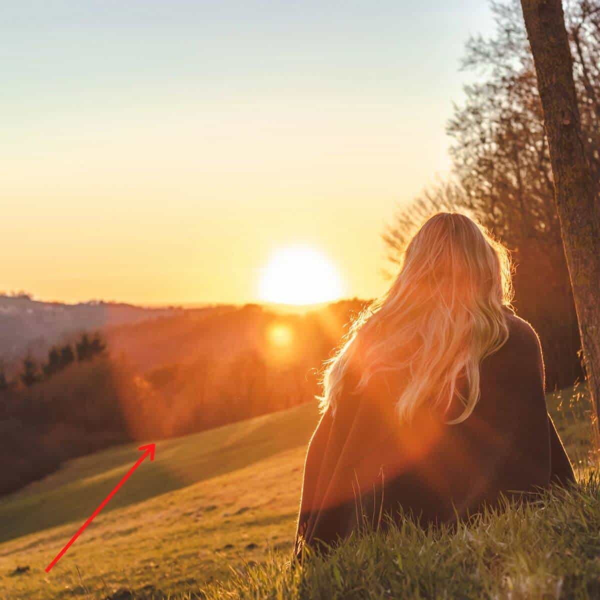 Person watching a sunset while sitting on a hill with an arrow pointing at the lens flare.