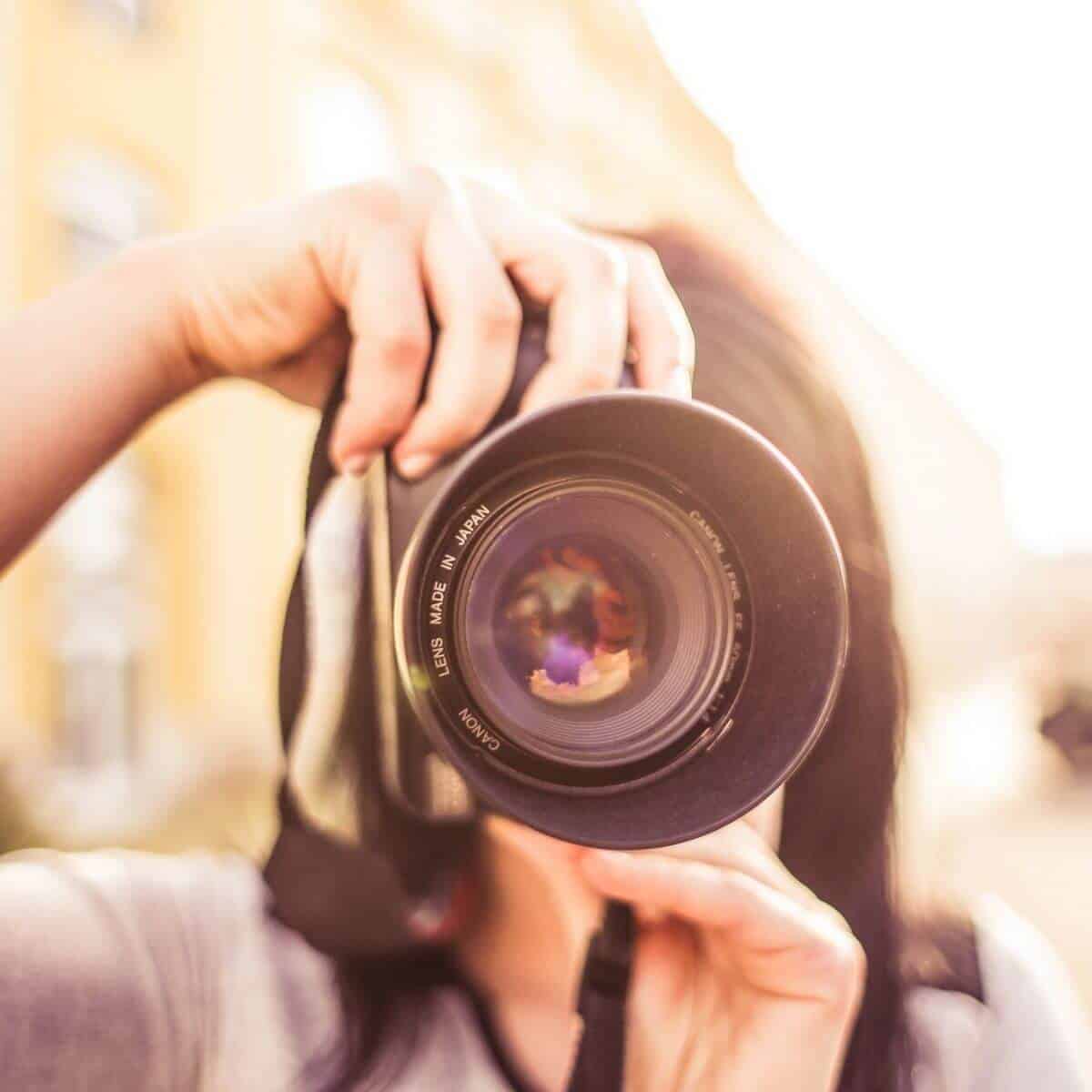 Selective focus on a camera lens while a person is taking a photo in the city.