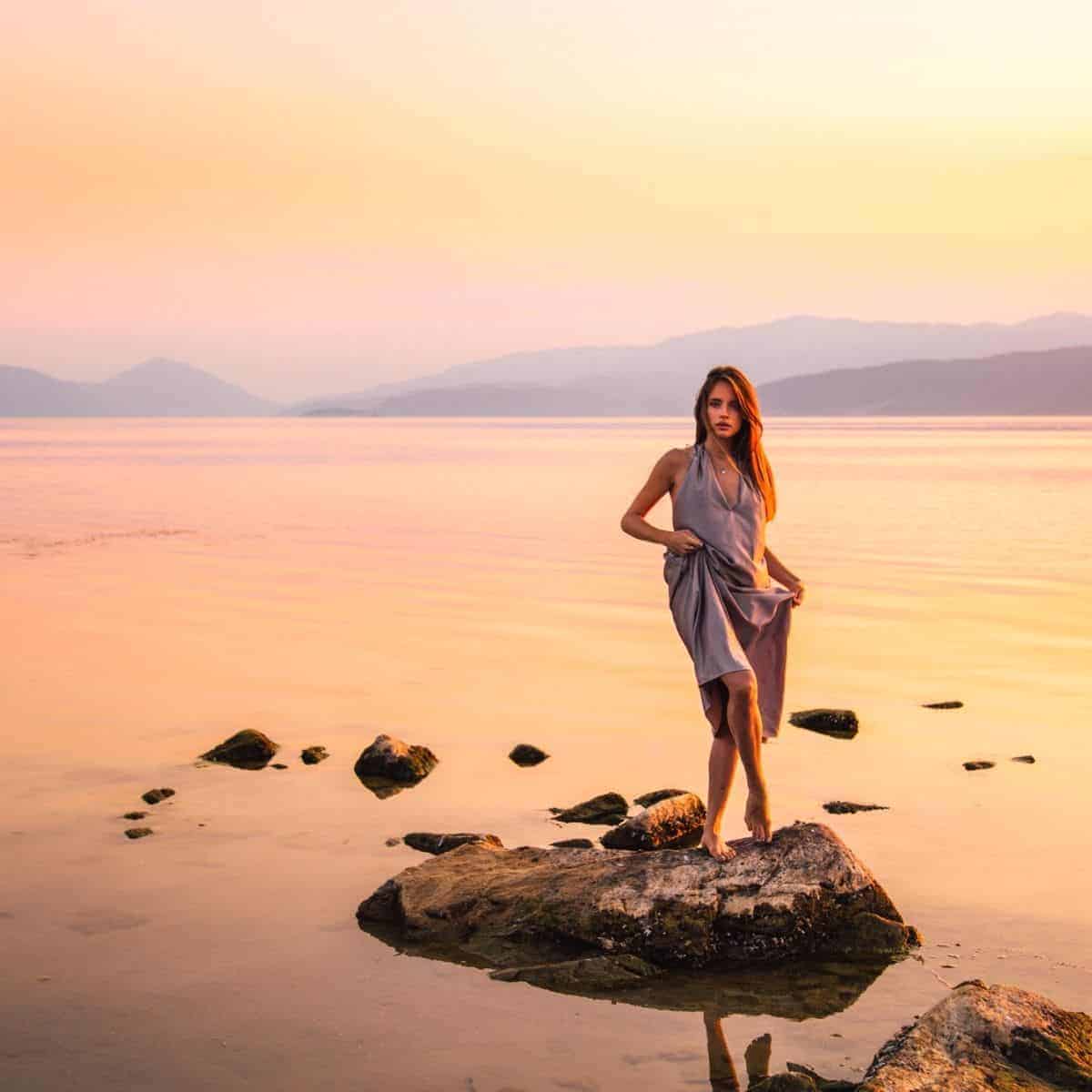 Person standing on a rock in the water during a sunset.