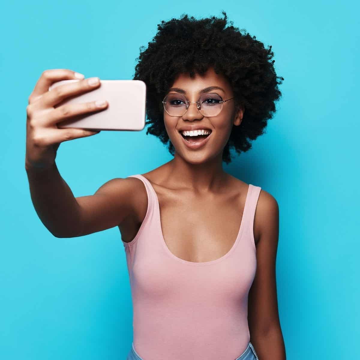 Woman wearing glasses and taking a selfie with a blue background.
