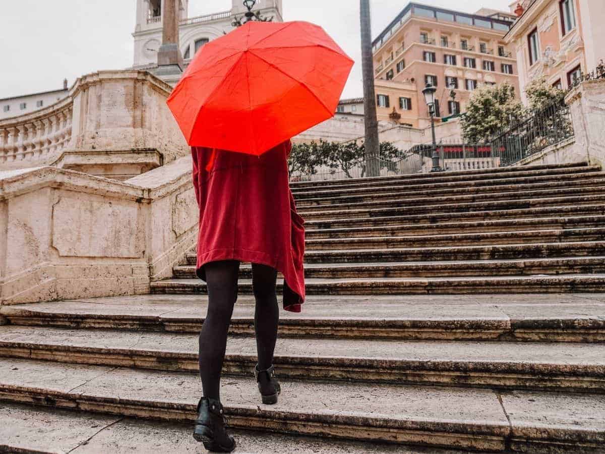 Person walking up stairs with a red umbrella.