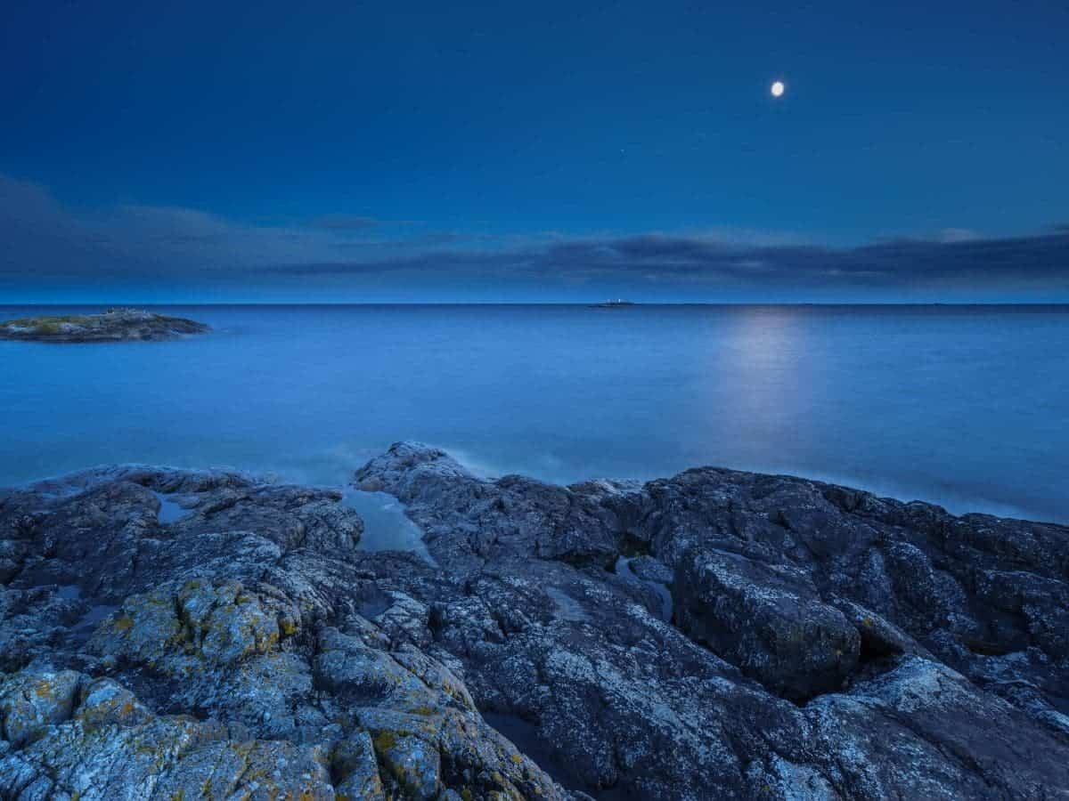Water, rocks, and the moon during the blue hour.