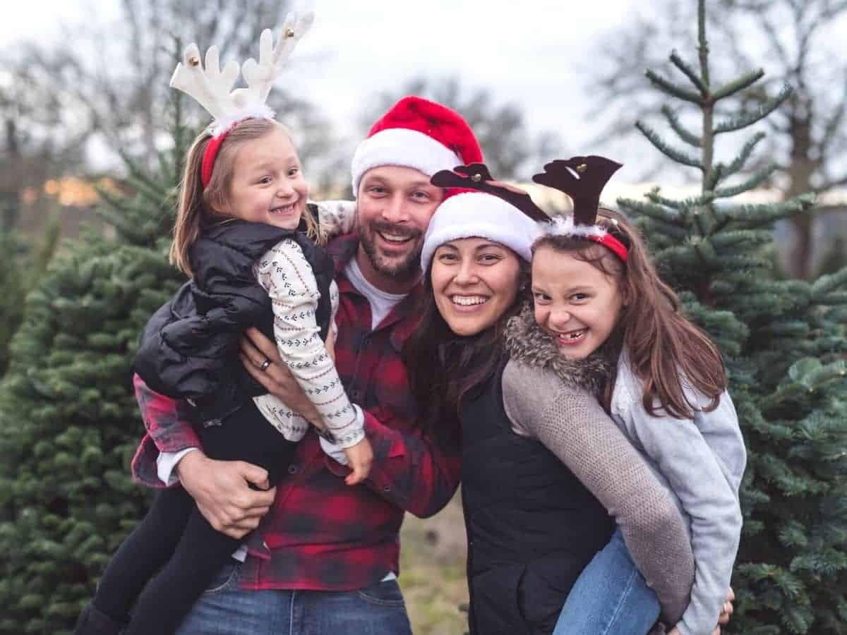 Family wearing Santa and reindeer hats at a Christmas tree farm.