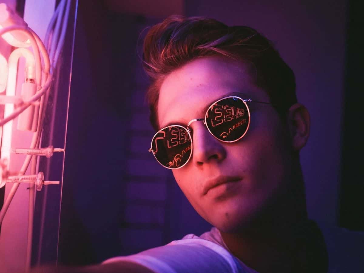 Headshot of a person wearing sunglasses at night and facing neon lights.