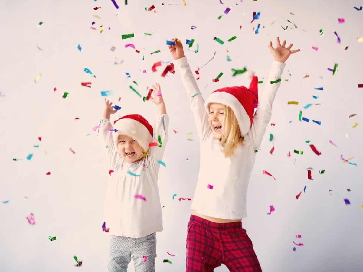 Kids wearing Santa hats with their arms up surrounded by confetti.