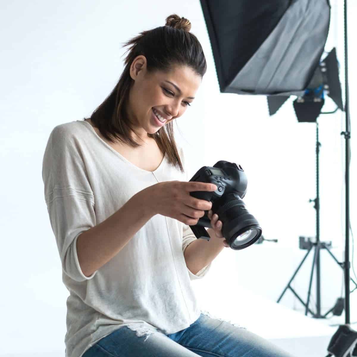 Photographer sitting down and looking at her camera in a studio.