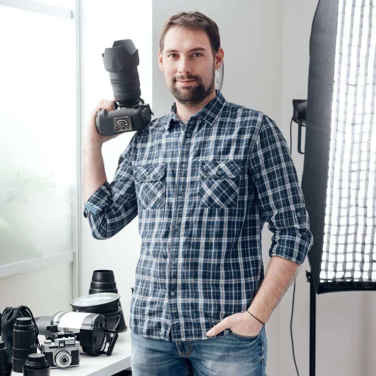 Photographer in a studio holding a camera next to lights, cameras, and lenses.