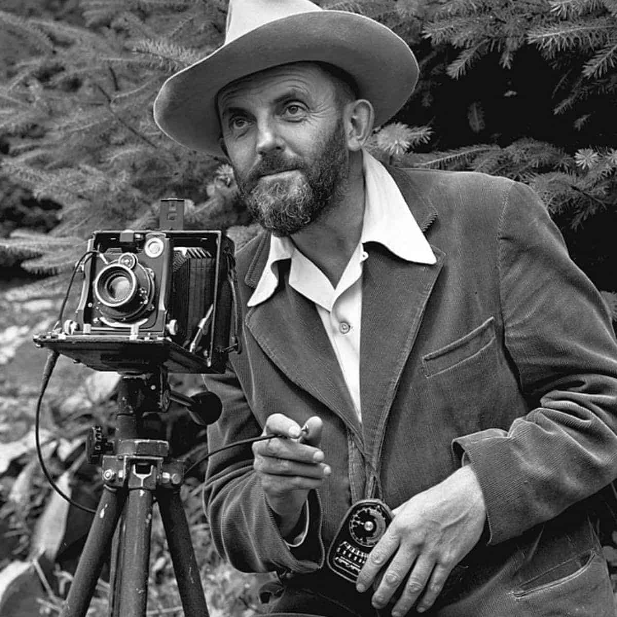 Ansel Adams with a camera in front of a tree.