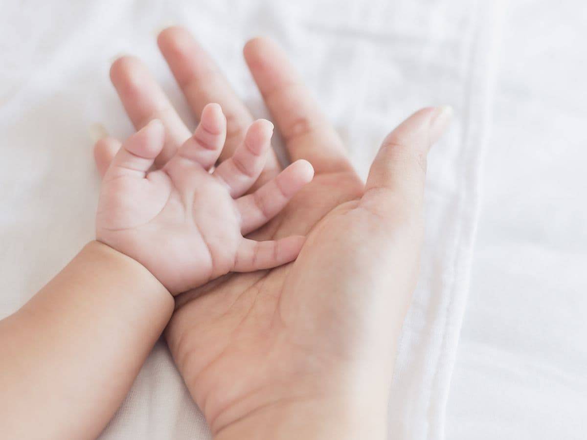 A baby's hand in their parent's hand.
