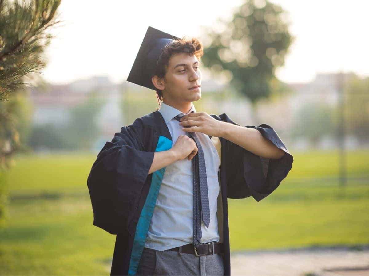 Graduate walking outdoors and adjusting their tie.