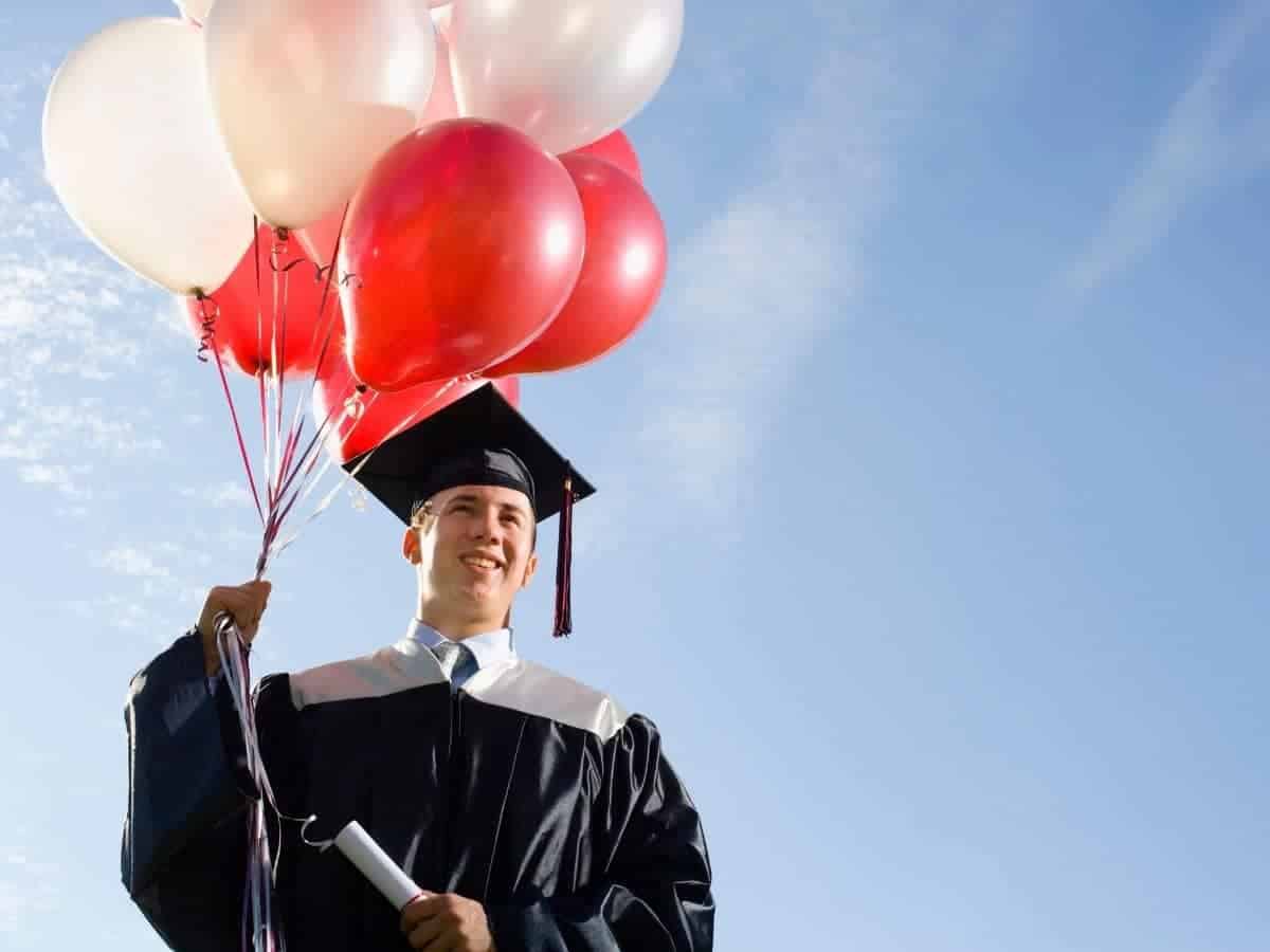 Graduate holding a diploma and balloons.