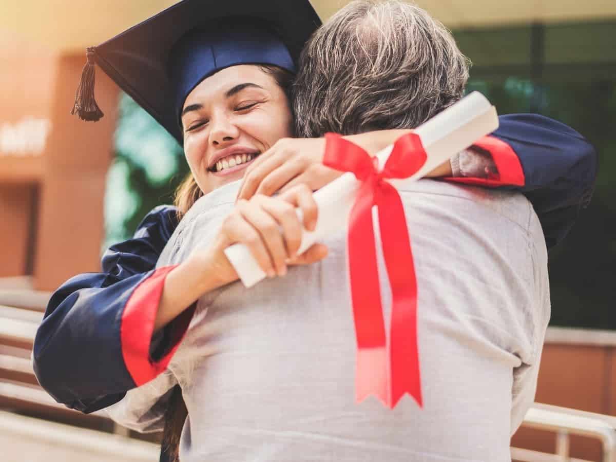 Graduate holding a diploma and hugging their dad.