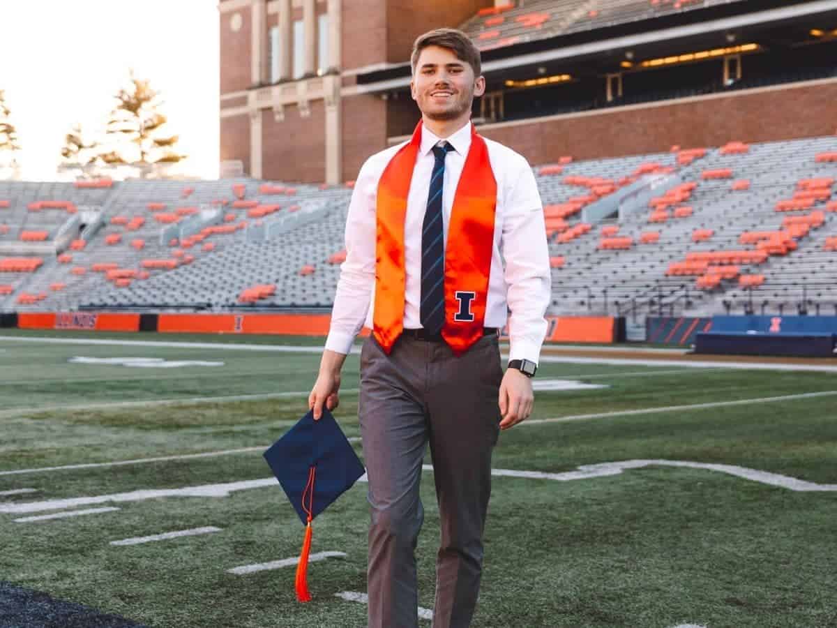 Graduate standing on a football field and holding their cap.