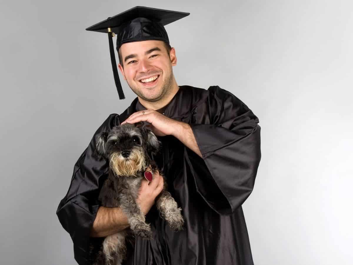 Graduate holding a dog and smiling.