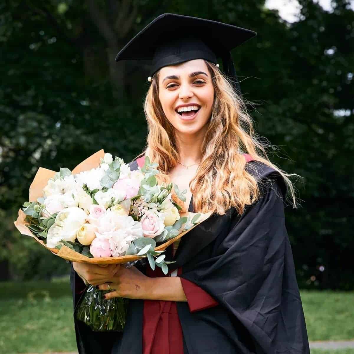 Graduate smiling and holding flowers outdoors.