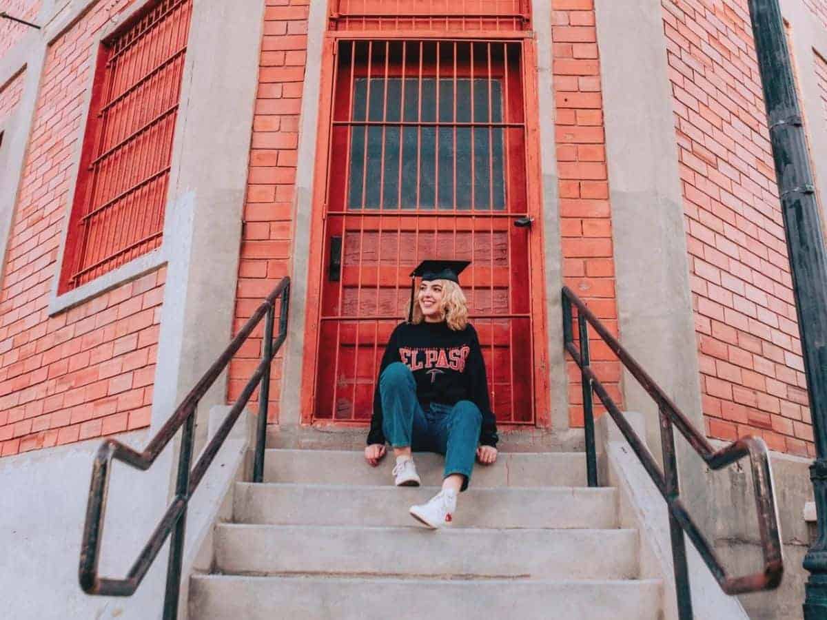 Graduate sitting on steps in front of a building.