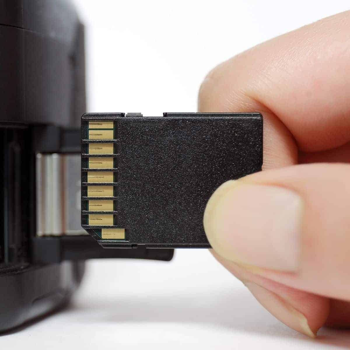 Hand holding an SD card near a camera.