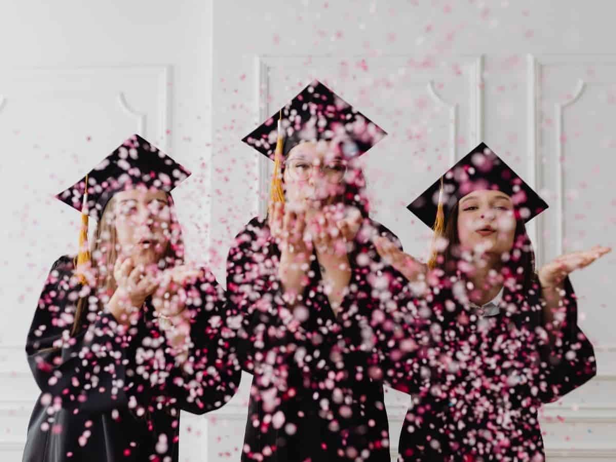 Three graduates blowing confetti.