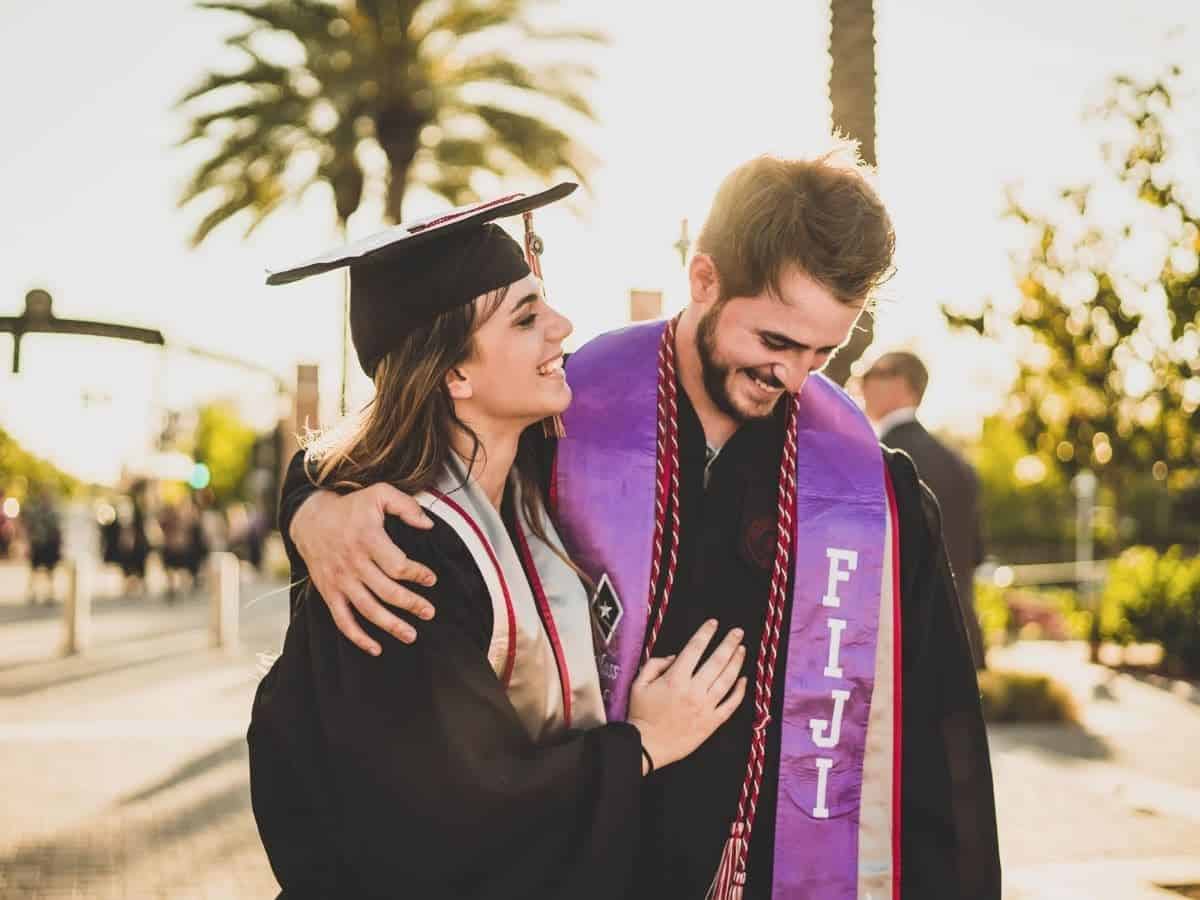 Two graduates outdoors with their arms around each other.
