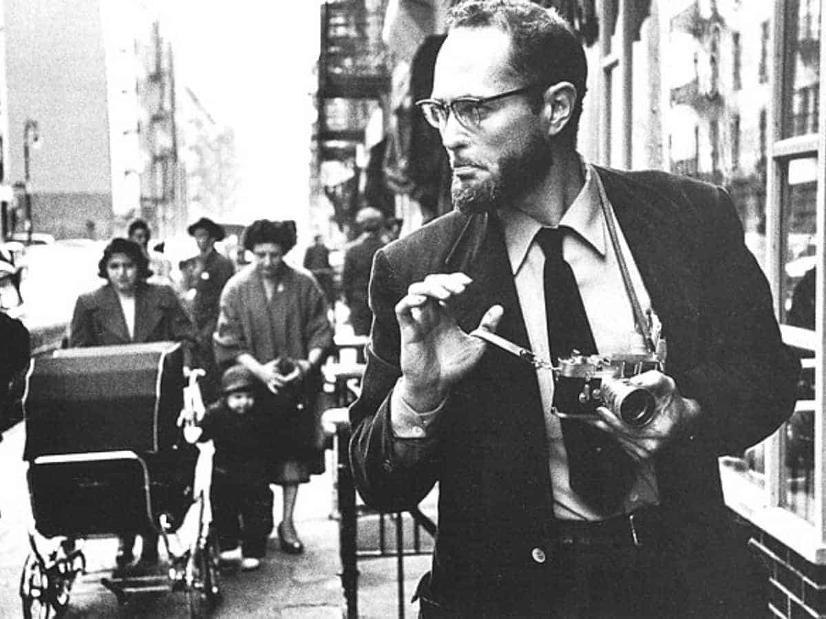 W. Eugene Smith walking on a sidewalk with a camera.