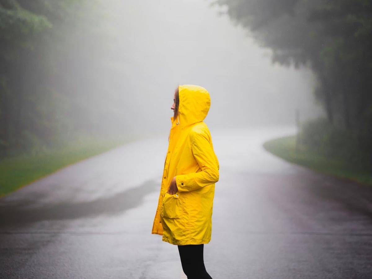Person wearing a yellow jacket and standing in the middle of a foggy road.