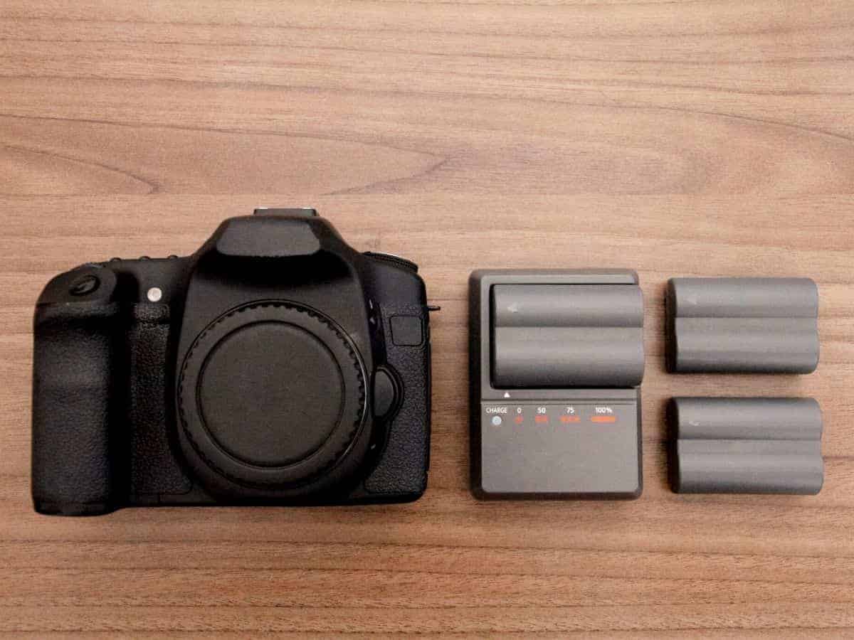 Camera, batteries, and a charger on a wooden table.