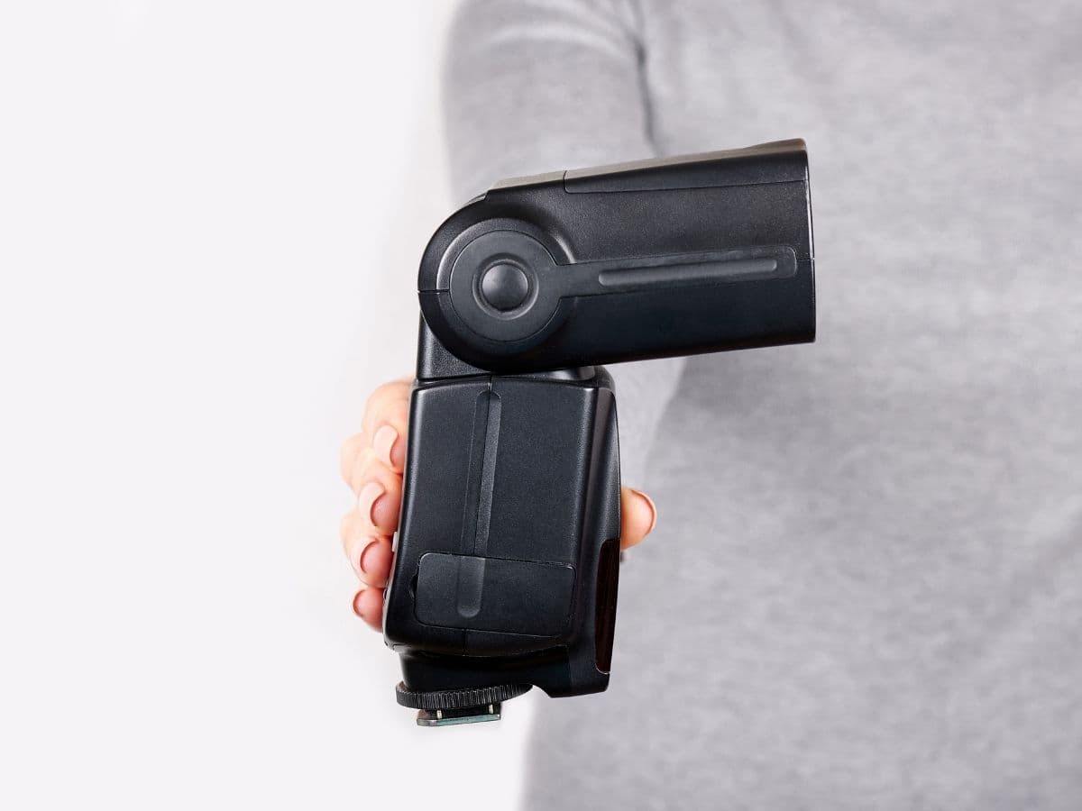 Person holding out an on-camera flash unit.