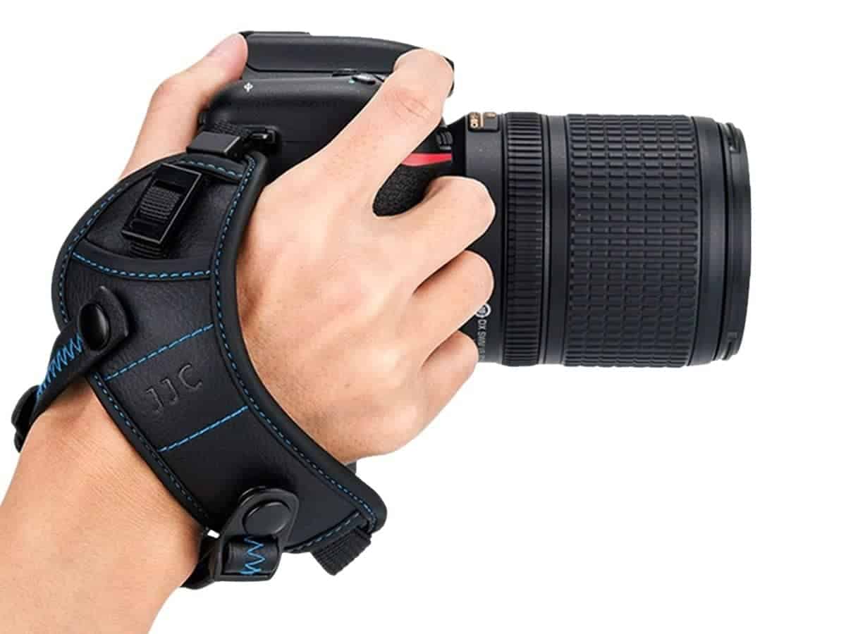 Person's hand holding a camera with a hand strap.