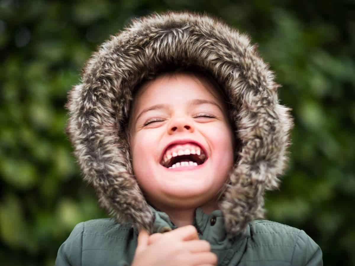 Kid laughing while wearing a fur hood.