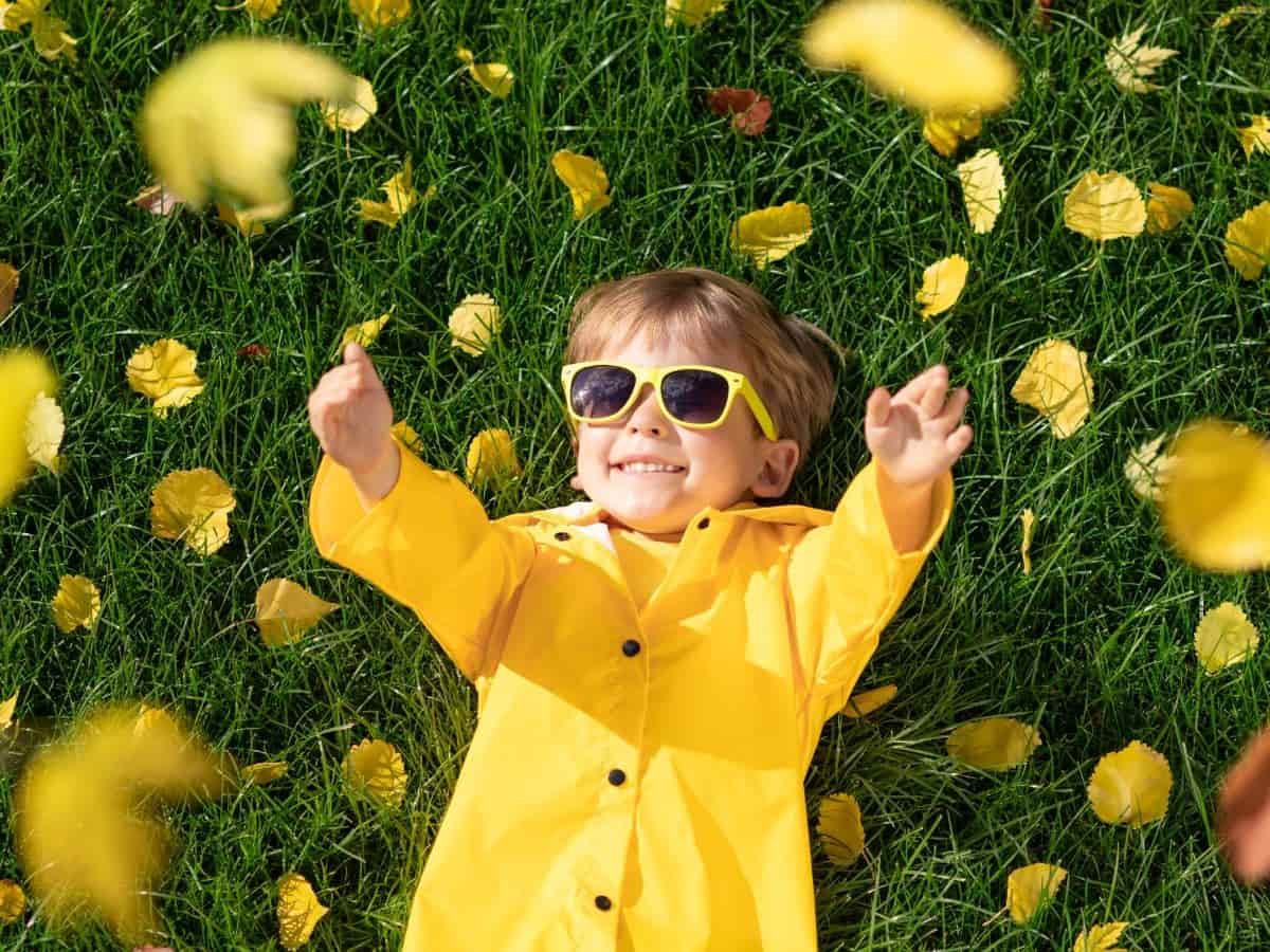 Kid laying on grass with sunglasses and surrounded by leaves.