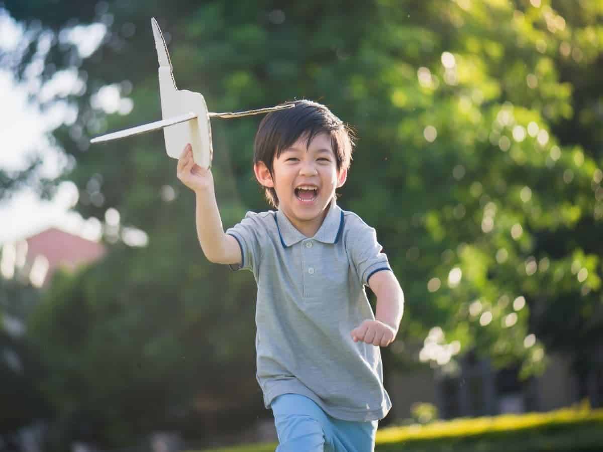 Kid running outdoors while holding a toy airplane.