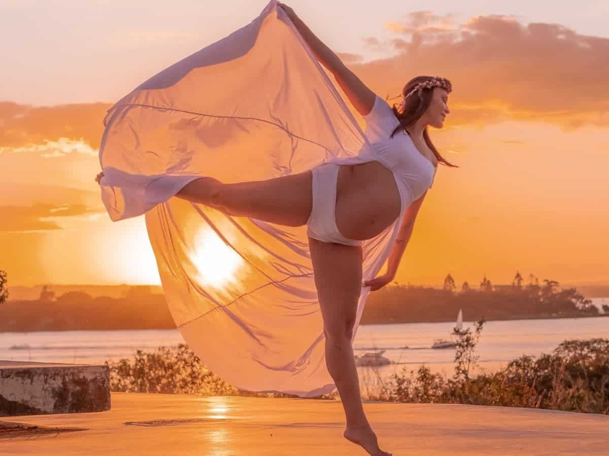 Pregnant woman dancing with a sunset behind her.