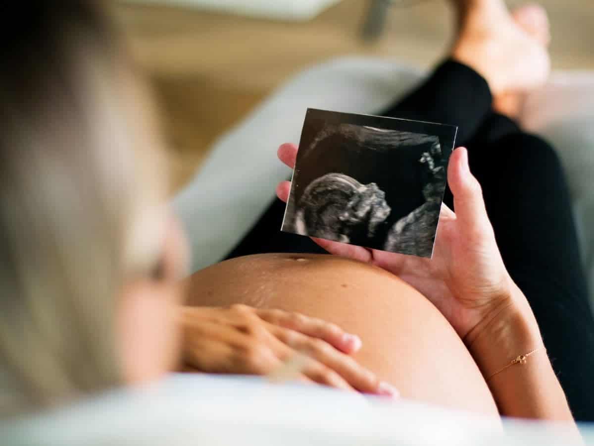 Pregnant woman sitting and holding an ultrasound picture.