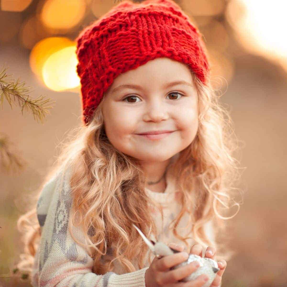 Child wearing a beanie and smiling outdoors.
