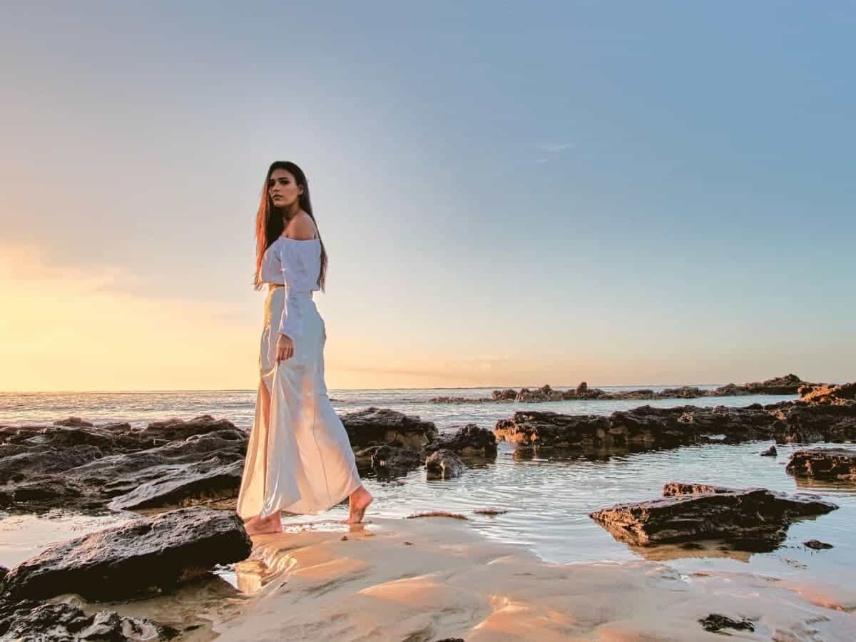 Tall woman wearing a dress and walking on a beach during sunset.