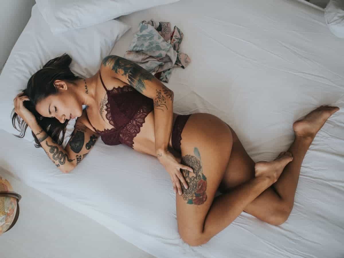 Woman with tattoos in lingerie on a bed.