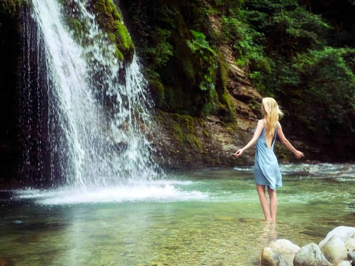 Woman standing in water facing a waterfall.