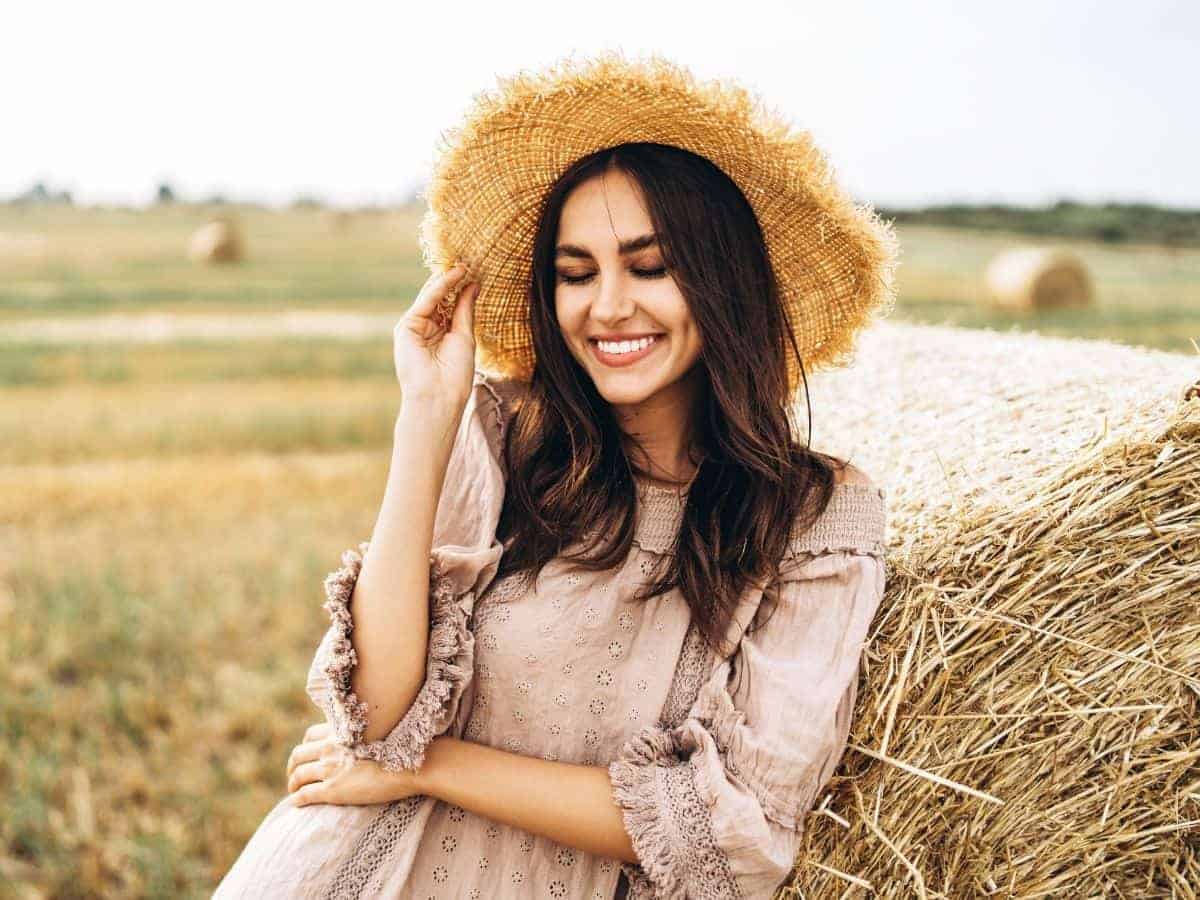 Woman wearing a straw hat and smiling in a field.