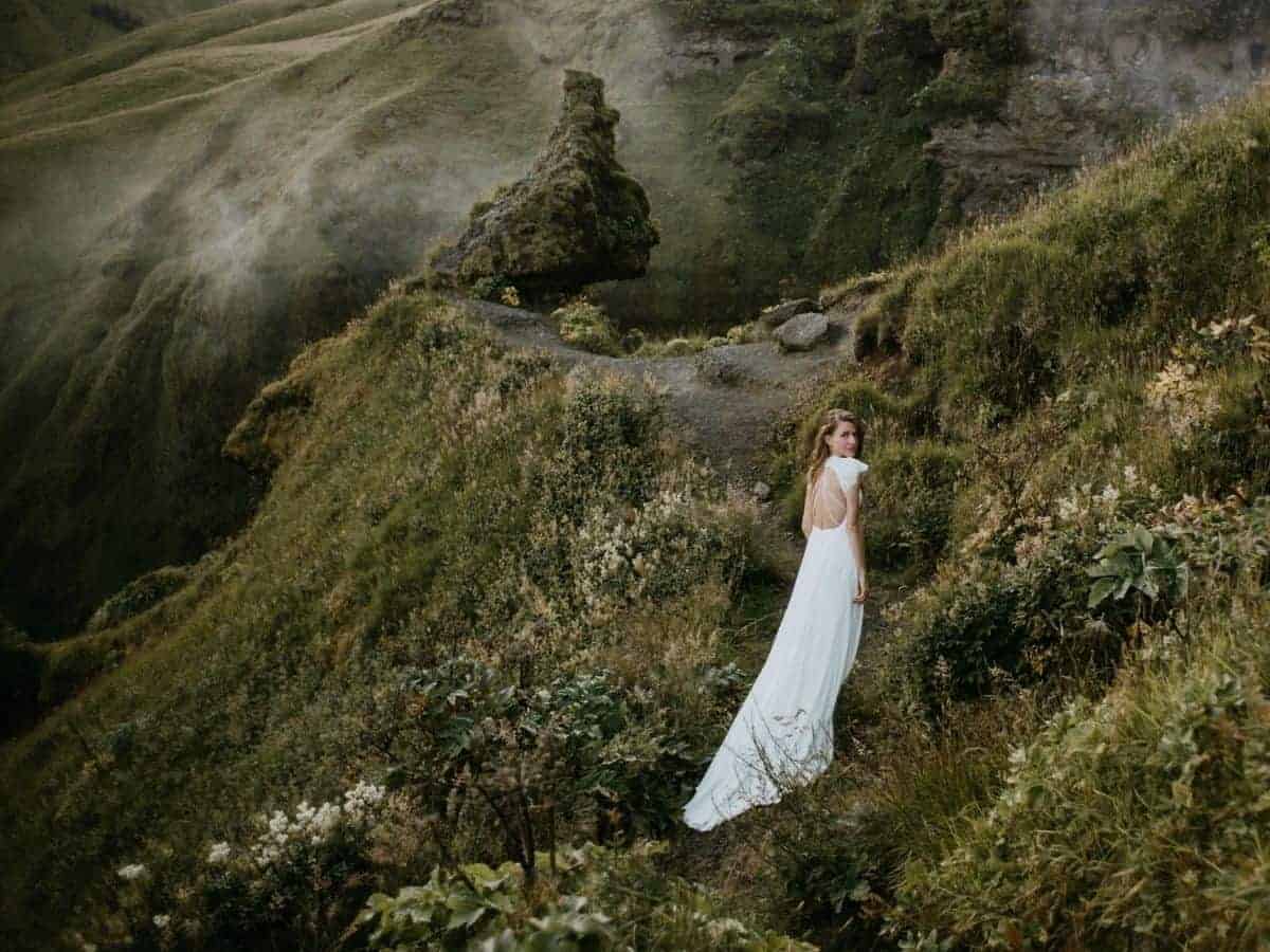 Woman wearing a dress and walking on a grass trail in the mountains.