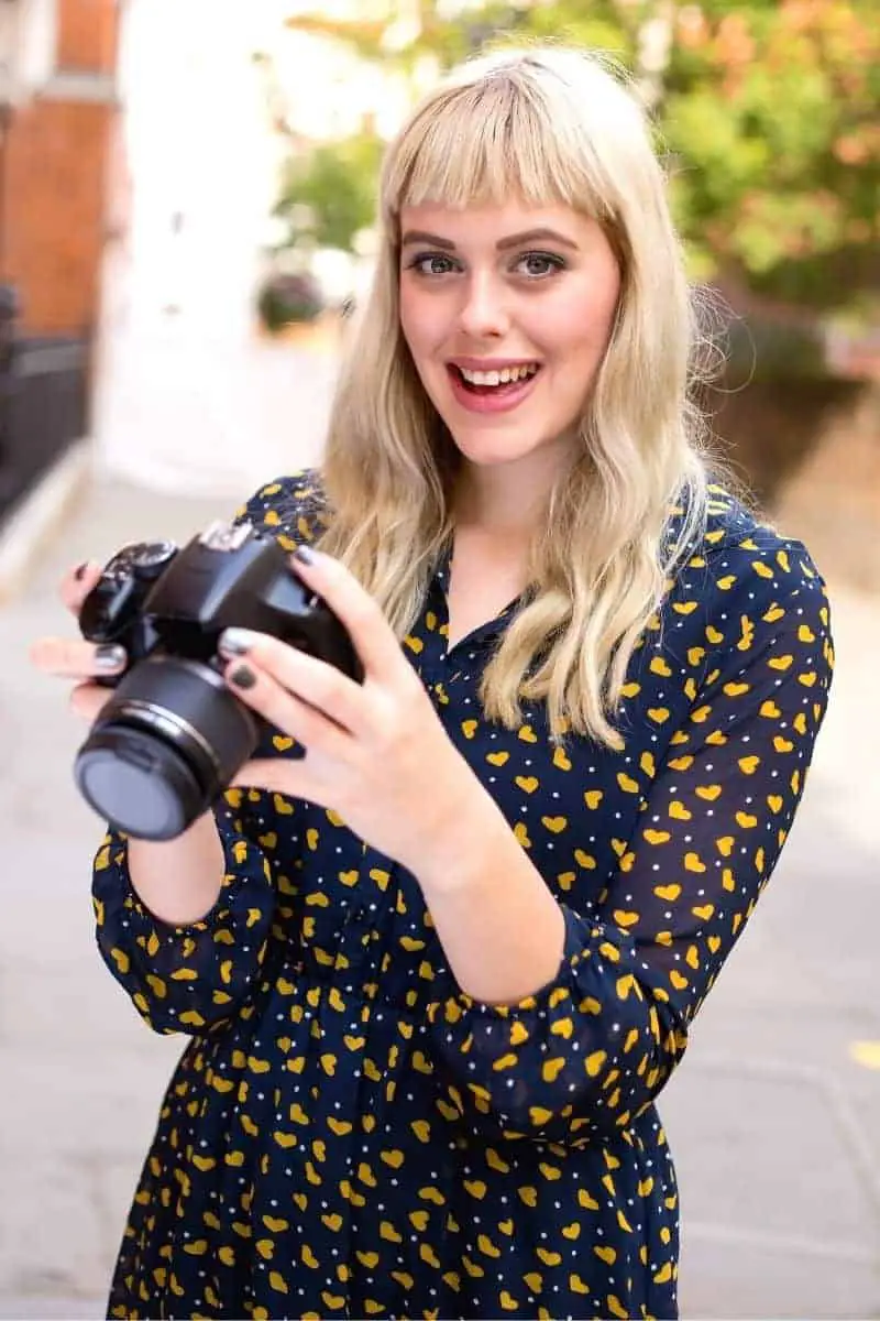 Photographer holding a camera and smiling outdoors.