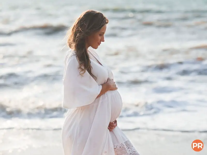 Pregnant woman in a dress standing at the beach.