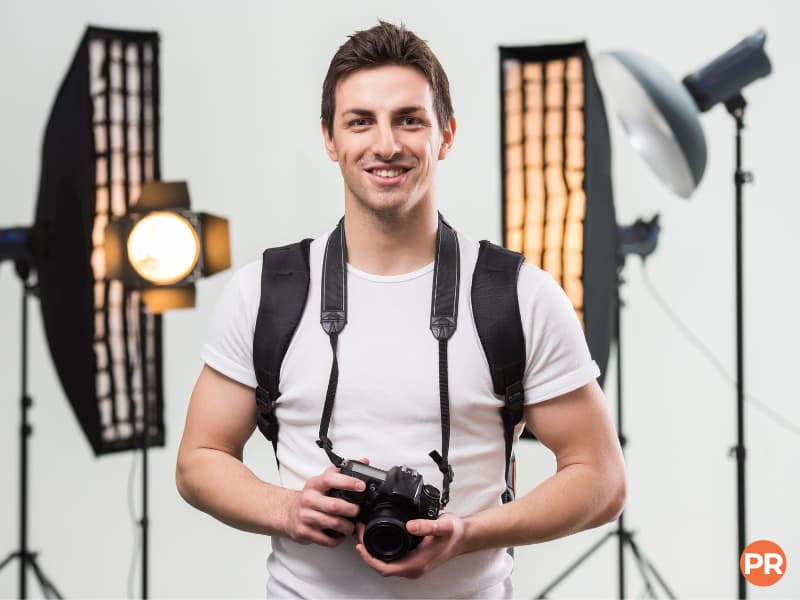 Photographer holding a camera and smiling in a studio.
