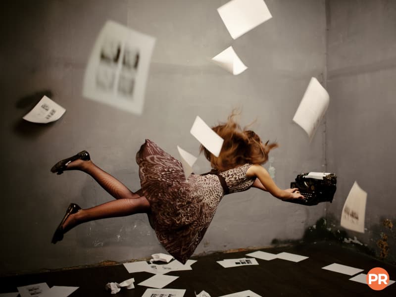 Person floating while using a typewriter and papers flying.