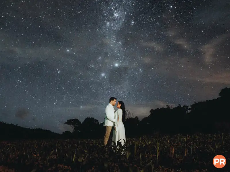 Couple hugging in a field under the night sky full of stars.