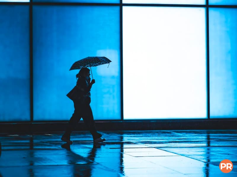 Person walking with an umbrella on a sidewalk at night.