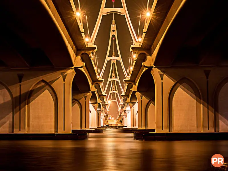Symmetrical view of a bridge and water at night.