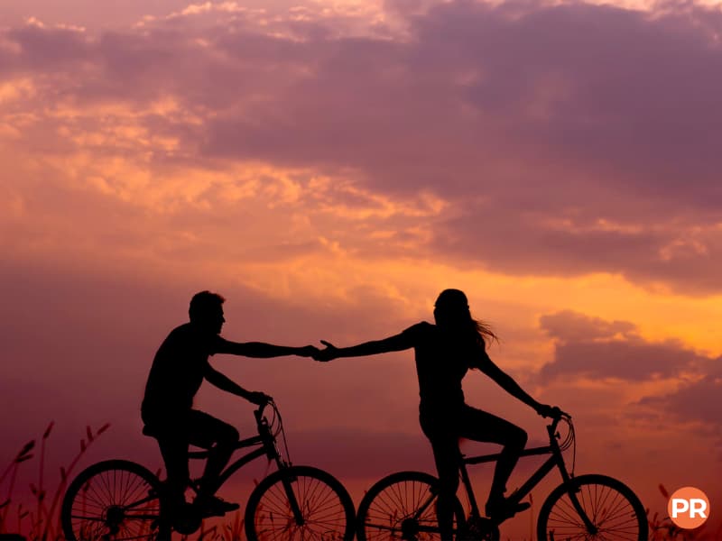 Silhouette of a couple riding bicycles and holding hands.