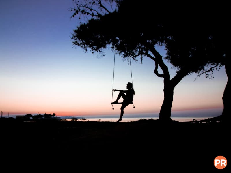 Silhouette of a person sitting on a swing near a tree.