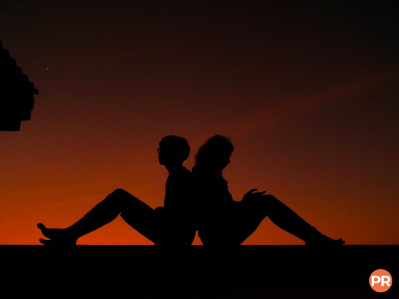 Silhouette of two people sitting back-to-back.