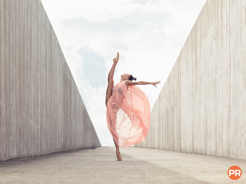 Ballet dancer posing between cement walls outside.
